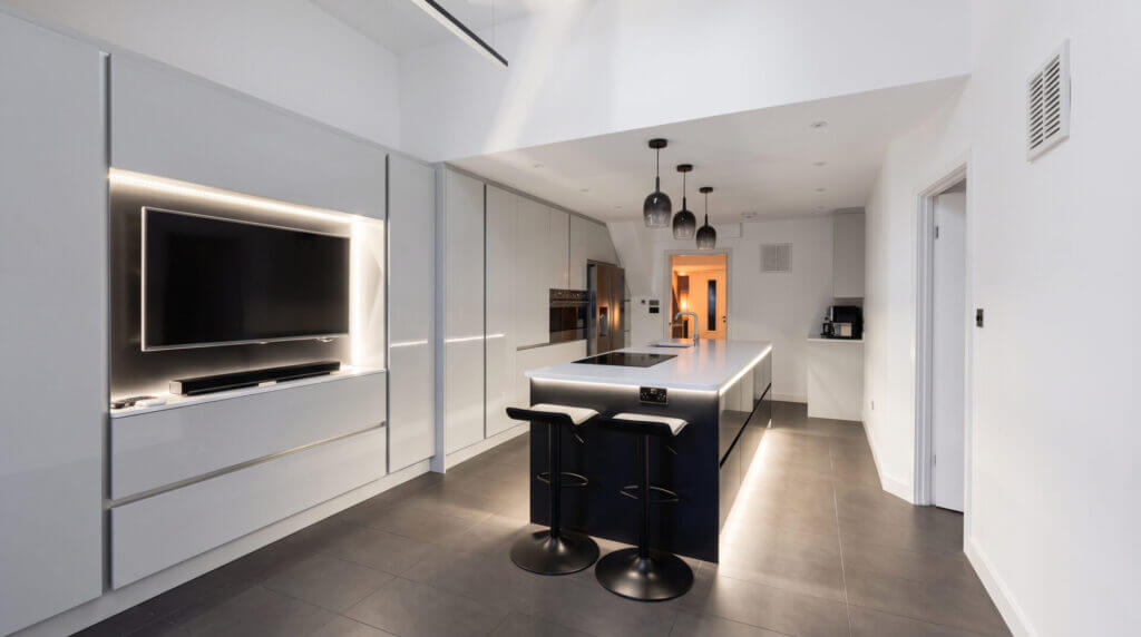White handleless kitchen with island, pendant lights and a built-in TV unit